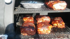 Seven succulent pork butts slow-cooking on the smoker, promising a feast of barbecue excellence