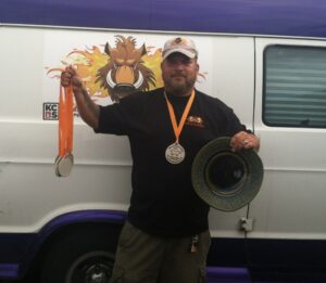 proudly holding gold medals from a BBQ competition, showcasing his culinary excellence