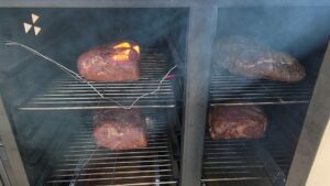 Four pork butts smoking in the grill, surrounded by flavorful anticipation.