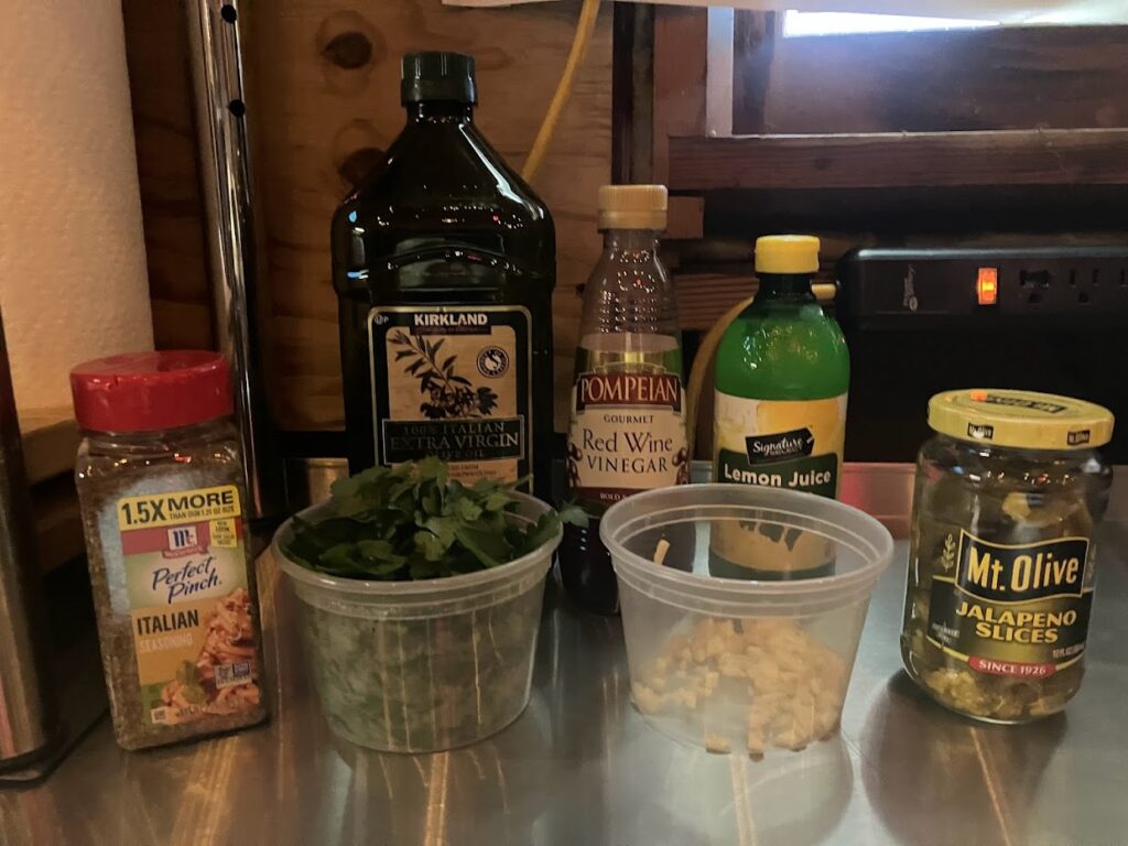 Italian Seasoning, Chopped Parsley, Olive Oil, Minced Garlic, Red Wine Vinegar, Lemon Juice, Jalapeno Slices ready to be blended in to a vibrant green chimichurri sauce