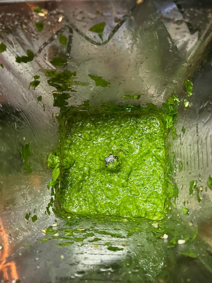 Freshly blended chimichurri in a glass blender, showcasing the vibrant green hues of herbs, garlic, and olive oil
